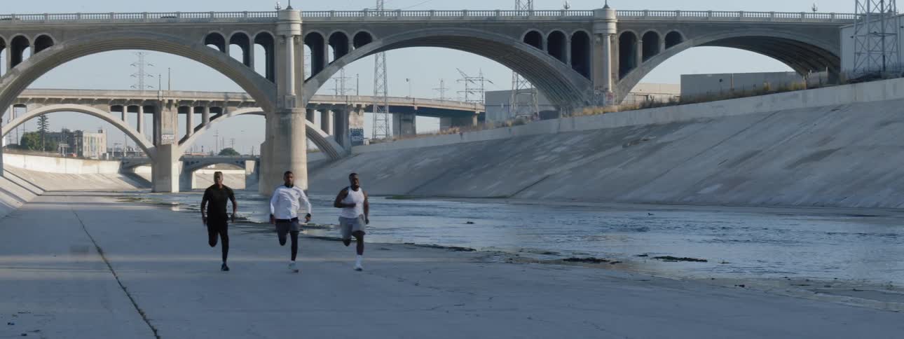 Three black men run along the los angeles river