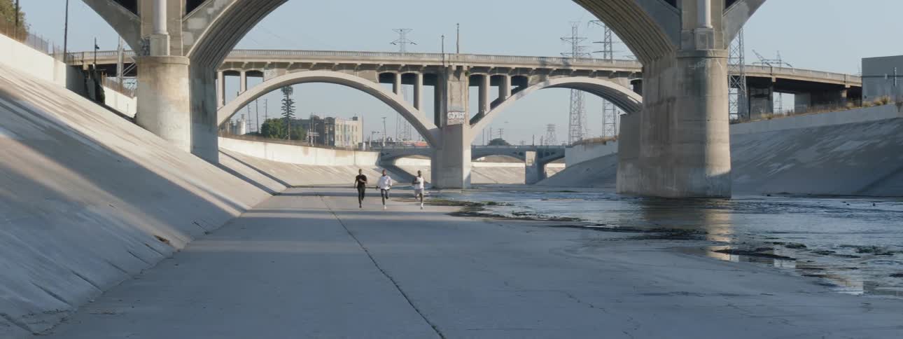 Three people run down a water way under a bridge