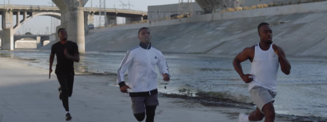 Three men run alongside water