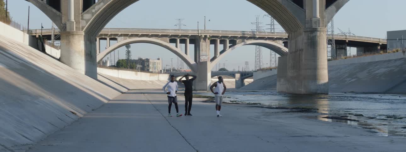 Three men walking down a sidewalk next to a river