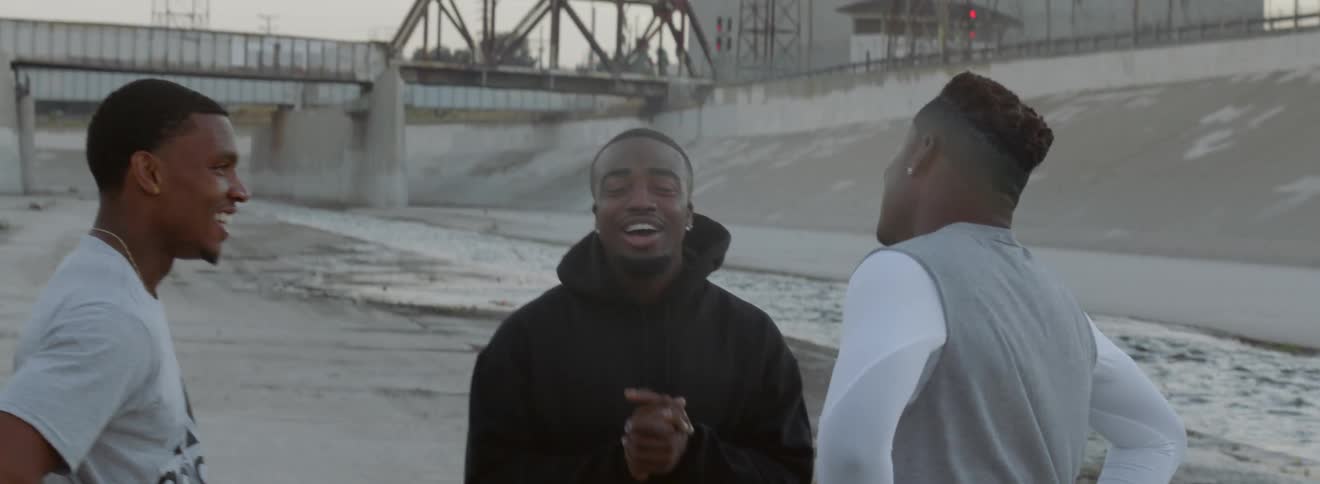 Three black men in athletic apparel stand outside talking and laughing