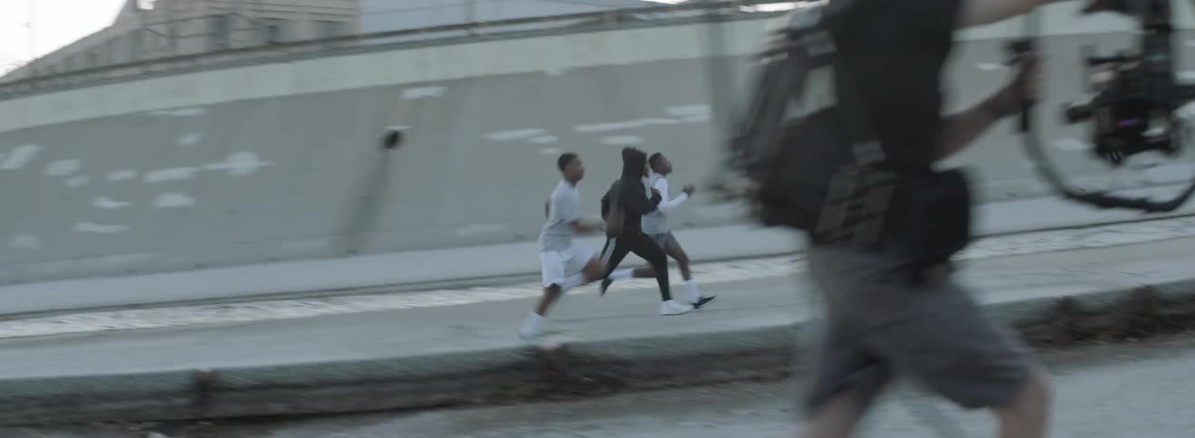 Three men run down a sidewalk as they are recorded