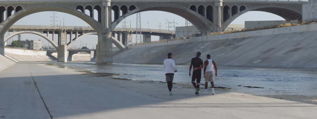 Three young men walk along a river bank