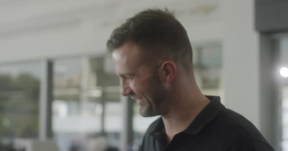 A man wearing a work shirt laughs and smiles as he talks with a person
