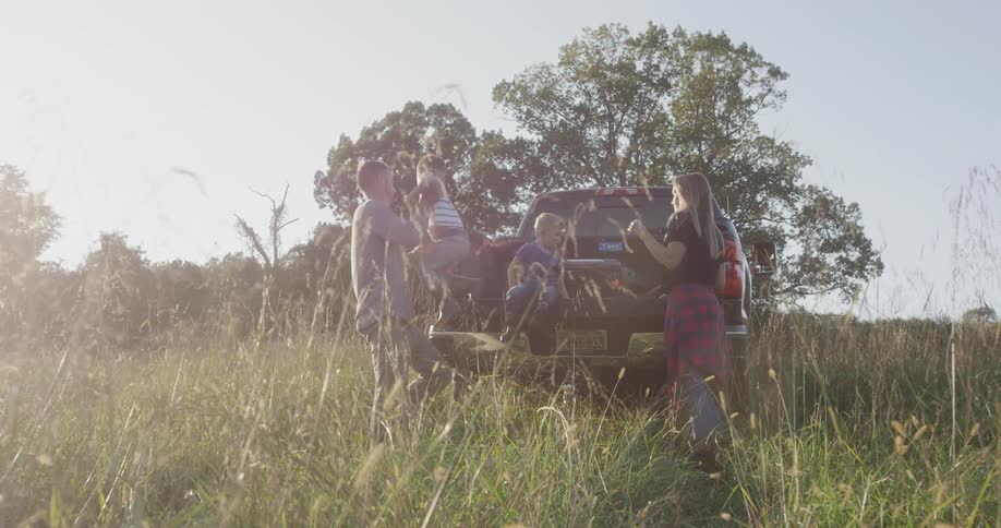 A dad picks up his son and places him on the tailgate next to his brother while mom looks on