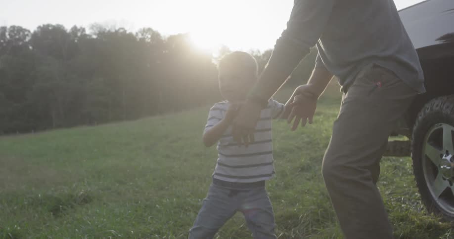A dad lifts his young son out of a pickup truck and puts him down in the grass next to his family