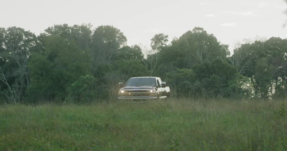 A pickup truck drives through a field in front of a forest
