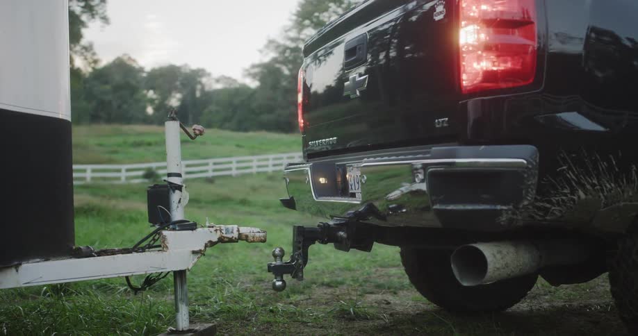Black chevy truck backing up to a trailer hitch in the country