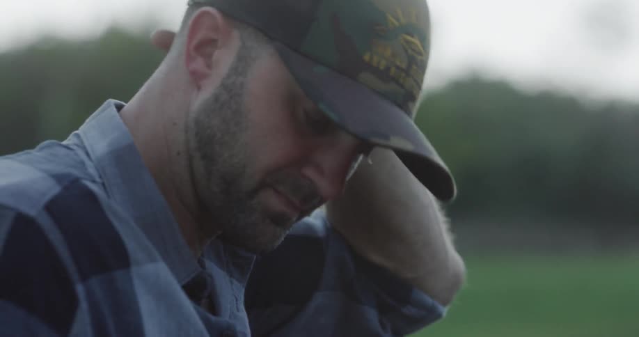 Man wearing cap and wristwatch looks down at car trunk on the grassland