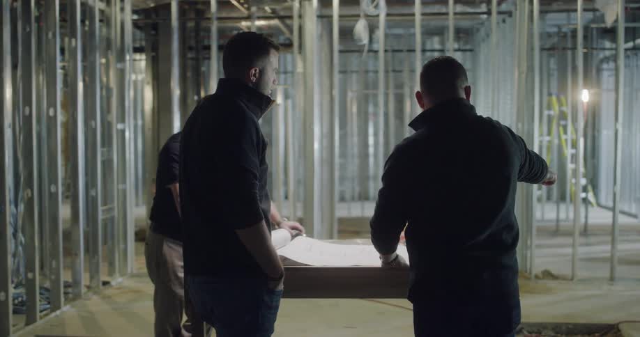 Three men talk inside a half built building