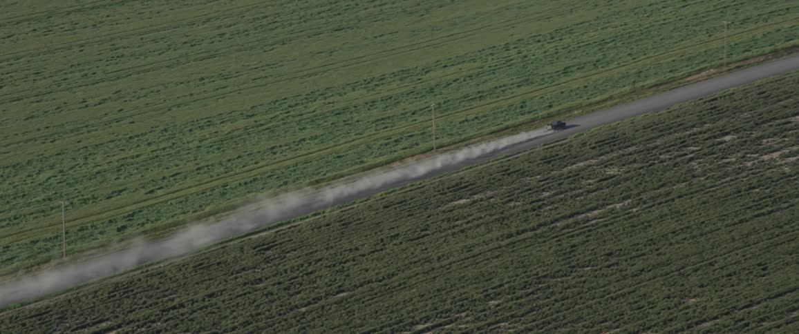 A truck drives down a dirt road between farm fields