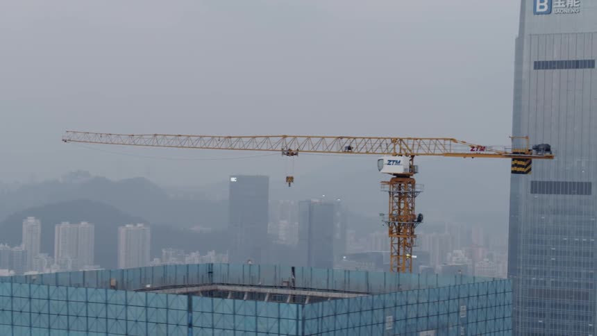 A construction crane sits at the top of a new skyscraper overlooking a city
