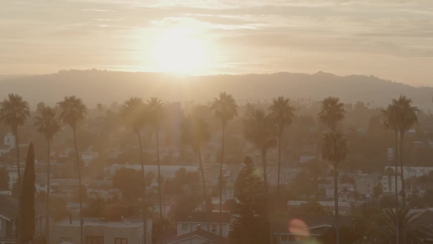 The camera looks out over a city with the sun in the background