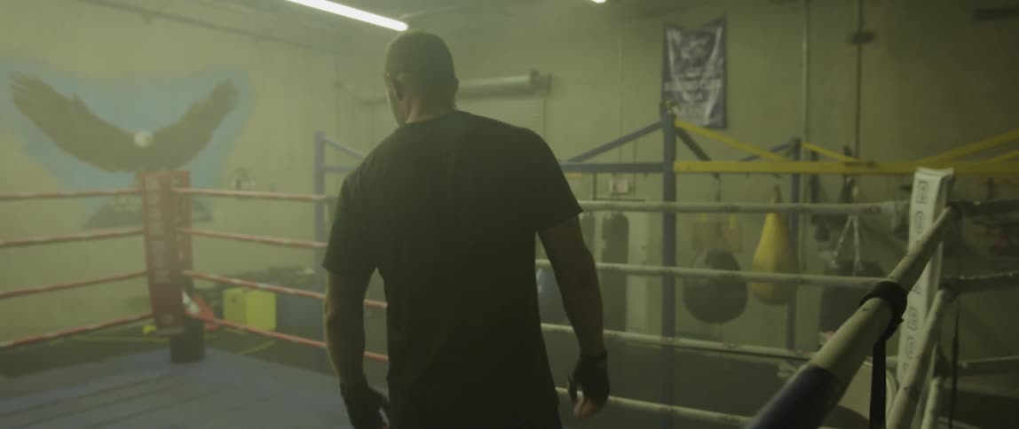 A man walking around a boxing ring in a small gym