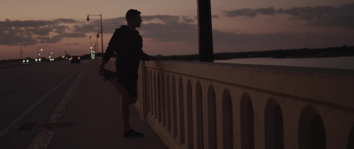 A white man stretches his legs while standing on a bridge