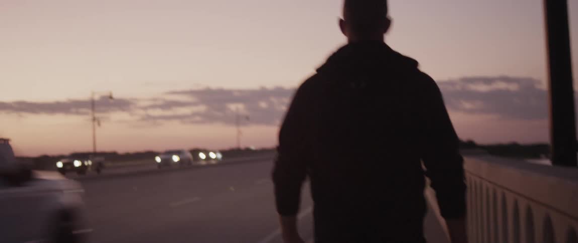 A white man walks down a sidewalk over a bridge