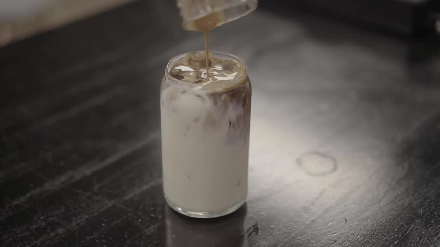 A shot of espresso is poured into a glass of milk