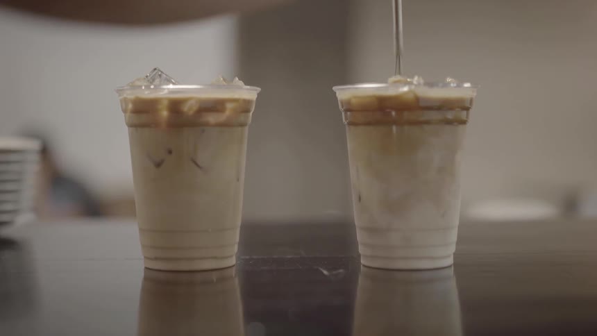 A person is using a metal whisk to stir an iced coffee drink in a cup