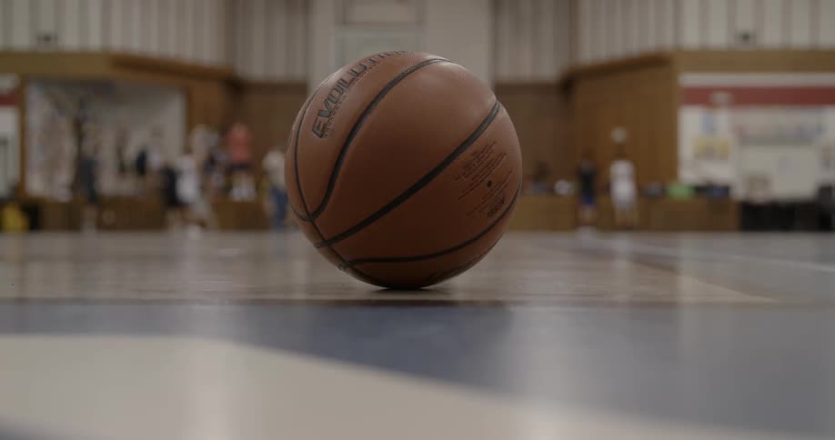 View of basketball on the gym floor while people play basketball in the background
