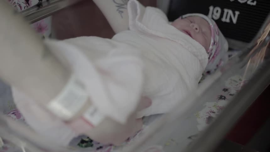 A woman places a newborn baby into a cradle in the hospital