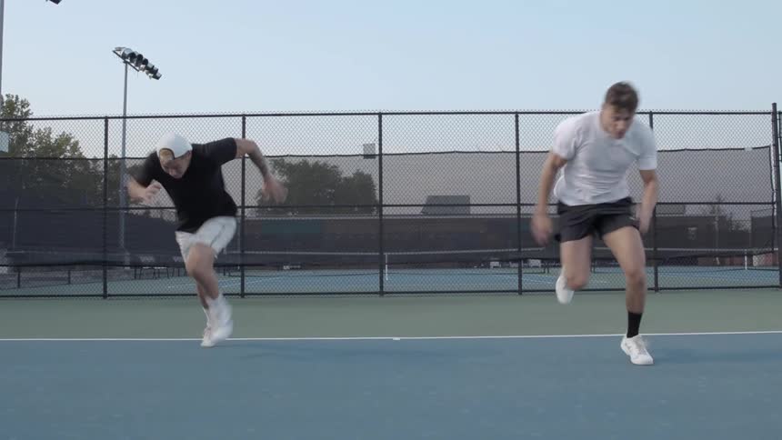 Two men stand at the white line of an outdoor court get set and sprint off in a race
