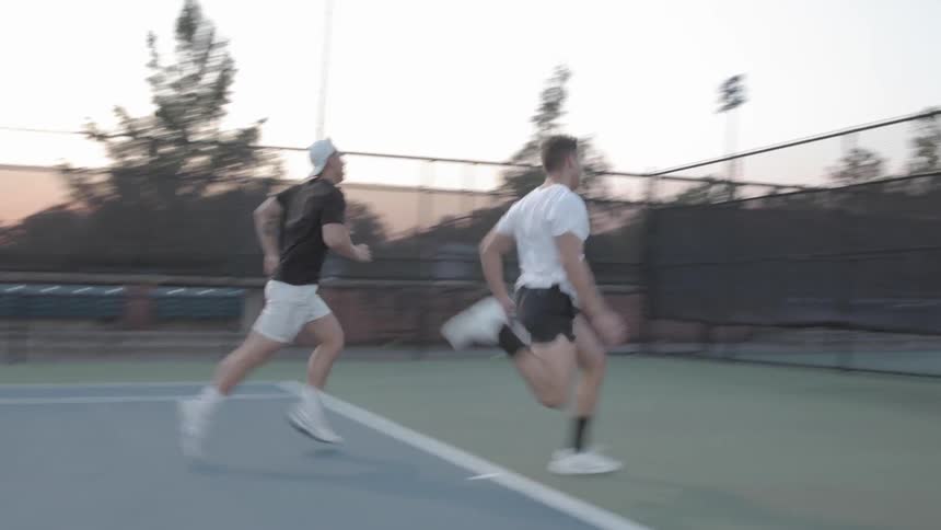 Two man race against each other in the tennis court at dusk