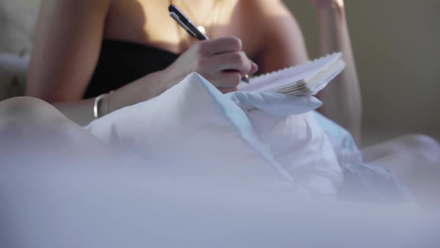 A woman is writing in a notebook in bed