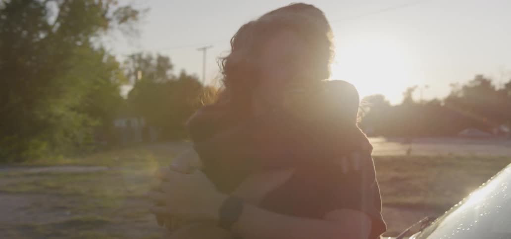 A couple stands next to a car and kisses