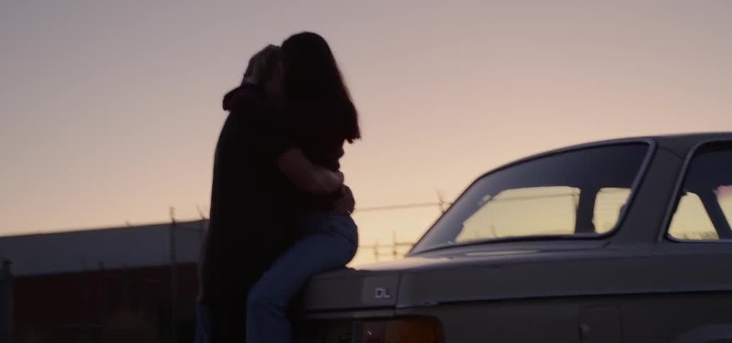 Man and woman make out on the hood of the car at dusk
