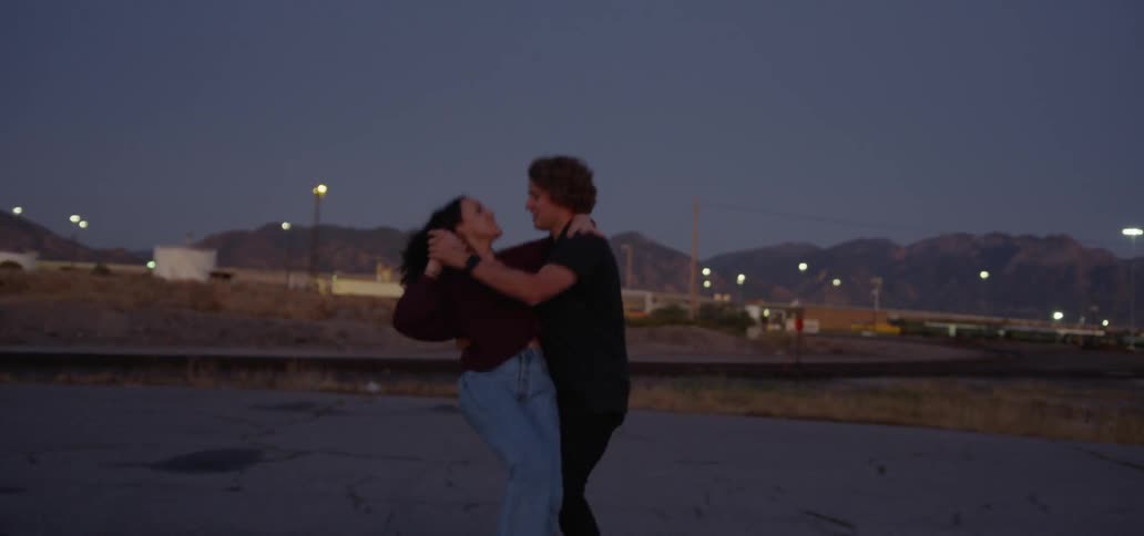 A man and a woman dance together outside in a parking lot at dusk