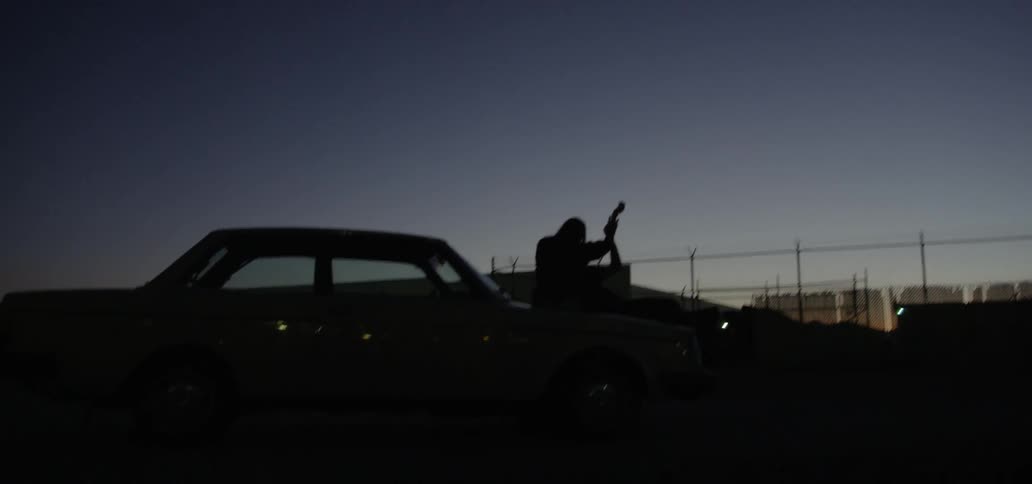 Silhouette of two people outside in the dark sitting on a car touching