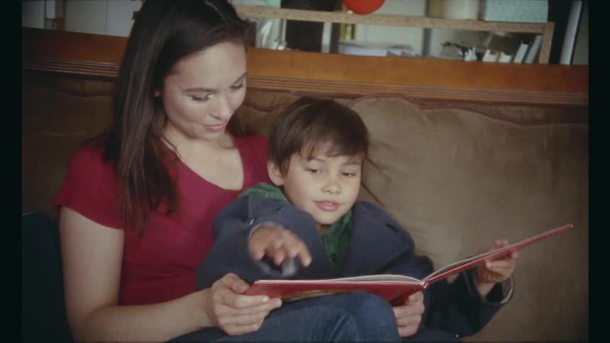 Mother and son read book together on sofa