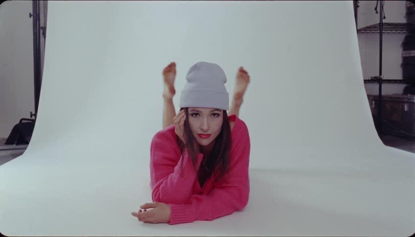 Female model in pink sweater and white hat poses while laying on stomach