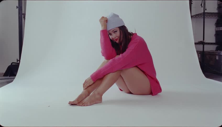 A model in a pink shirt and beanie hat poses at a photo shoot