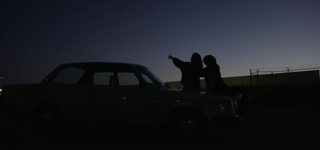A man and woman sitting on a car in the dark looking at the stars