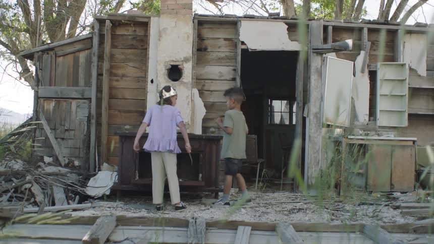 Two children play make believe outside abandoned shed