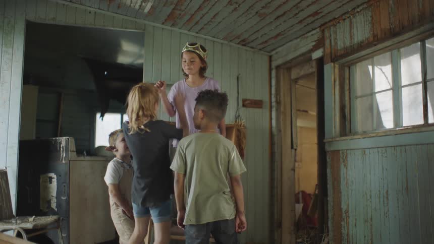 A girl standing on a chair with a crown pointing and playing with other children