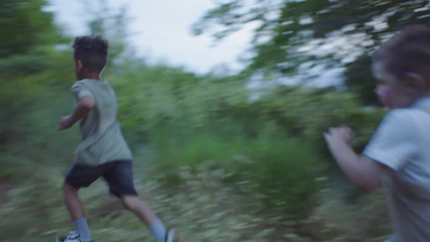 Three children run on a grassy path towards the forest