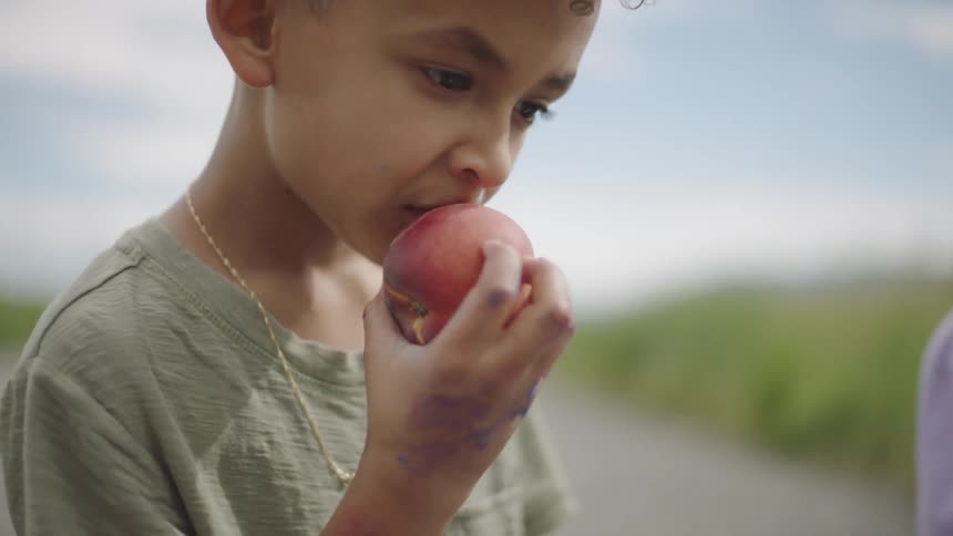 Young child nods and bites into peach outdoors