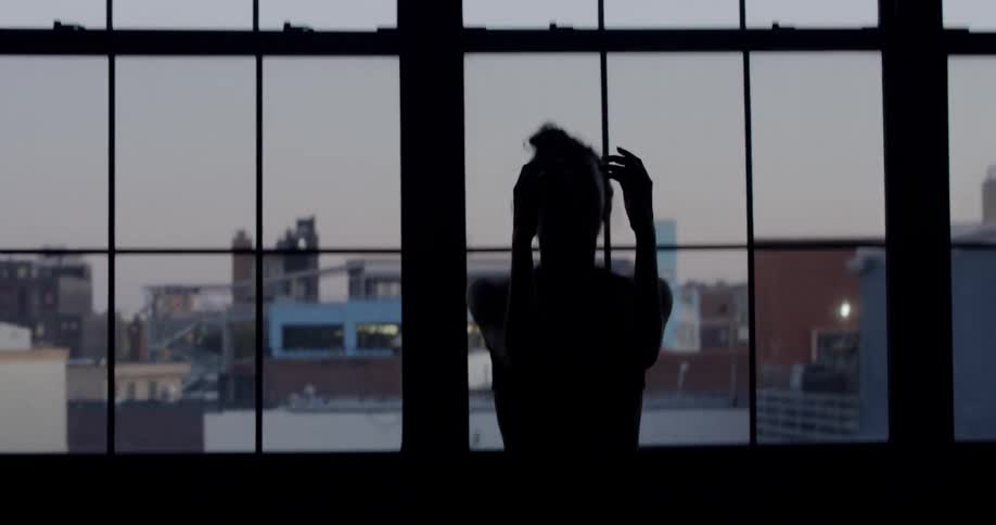 A young woman performs some dance moves inside a darkened room in the city