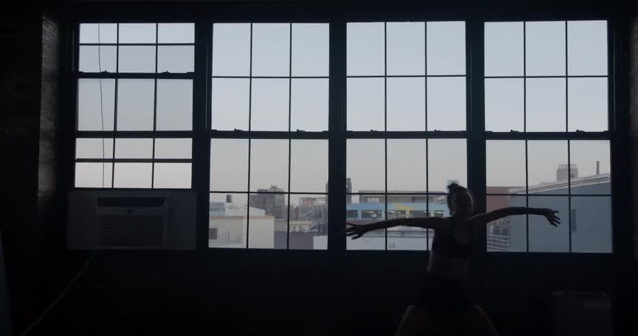 Modern dancer dances in front of large industrial windows that look out onto the city in a studio during the day