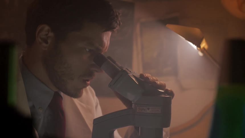 Scientist looks into a microscope with a confused expression