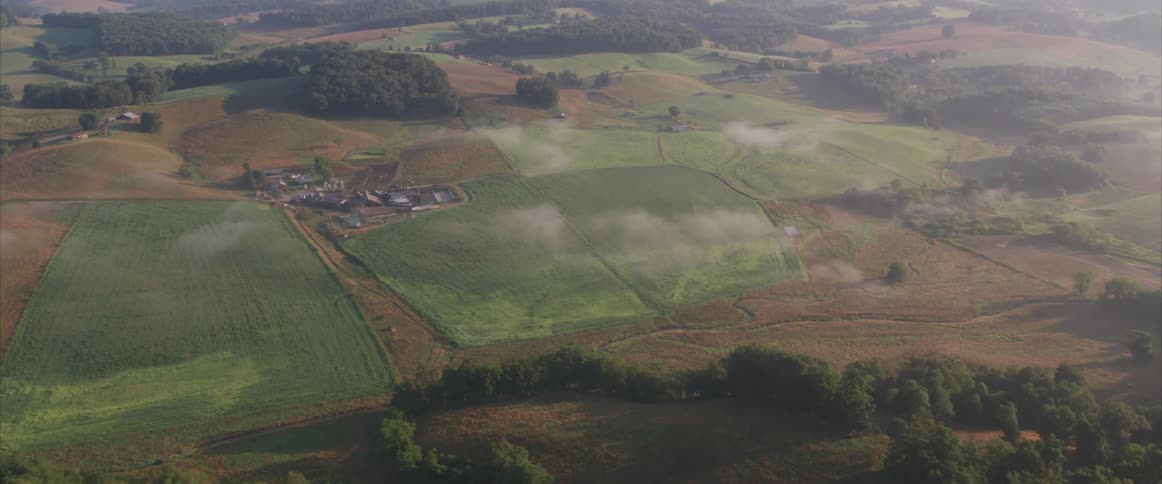 The camera flies over rolling hills full of grass and trees