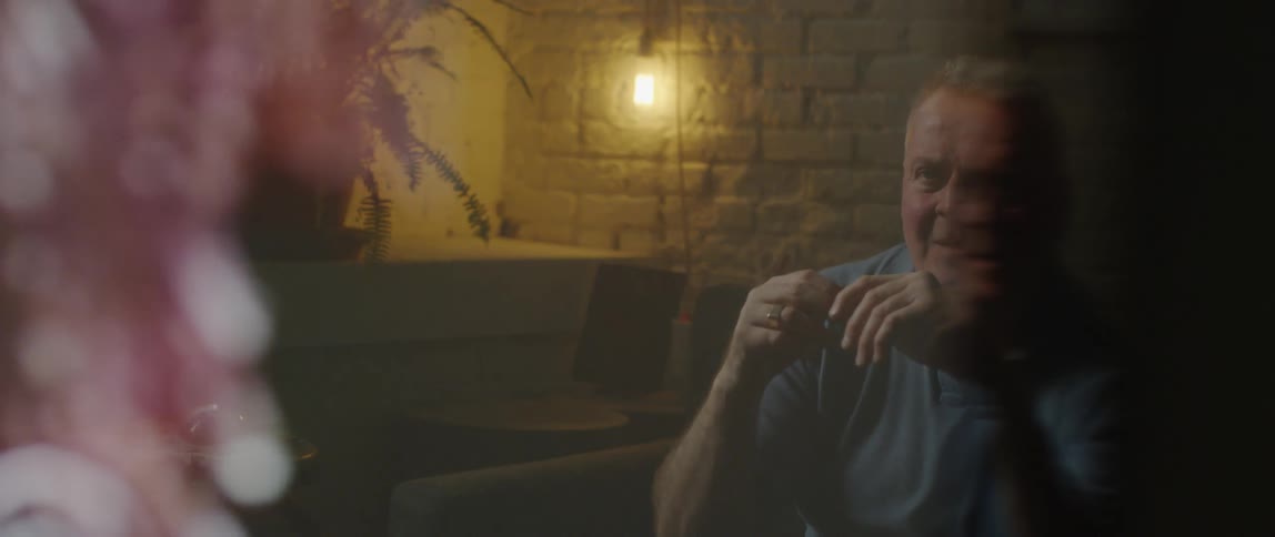 A man is sitting in dimly lit room and with great interest sits and stairs a recording of which a partial reflection can be seen