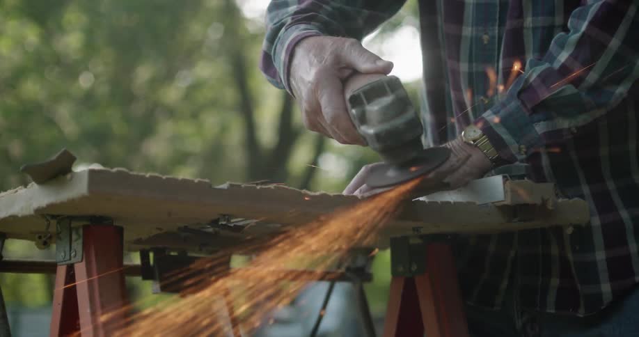 A white male using an electric saw outside on a workbench