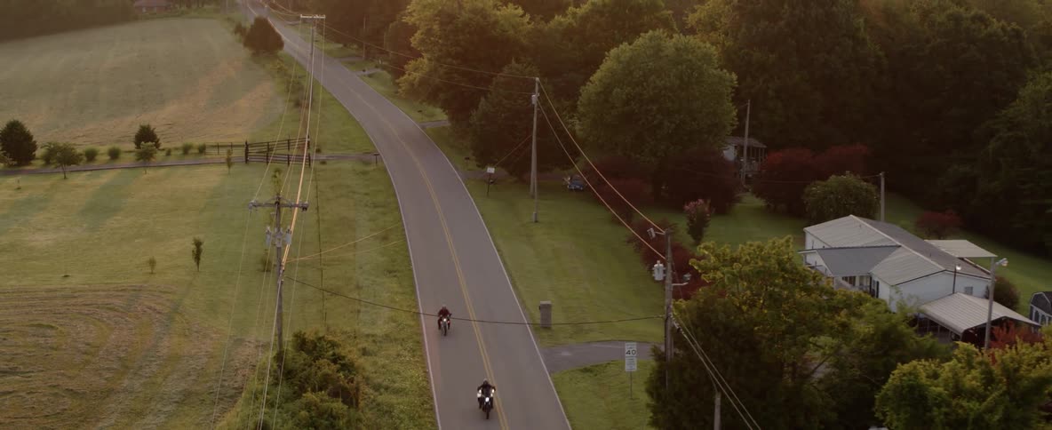 Two motorcycle ride along highway among forests and farms