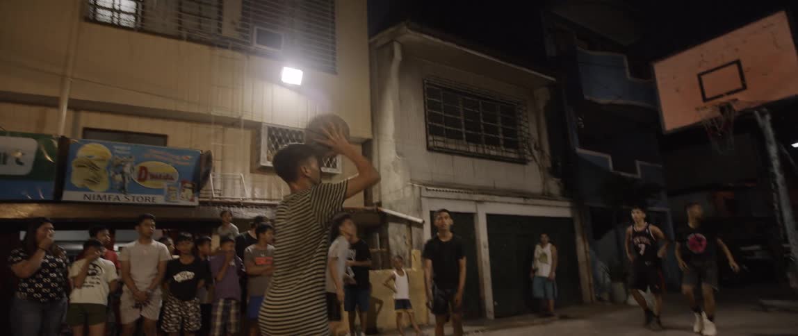 Crowd in poor neighborhood watching teenage boys play basketball