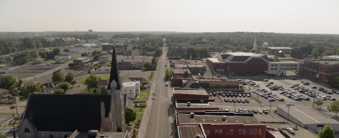A wide street cuts straight through a town center with a church buildings and parking lots