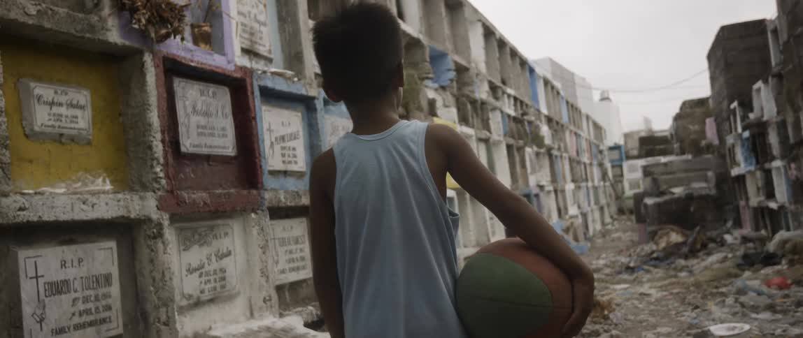 Boy stands with basketball among debris in cemetery