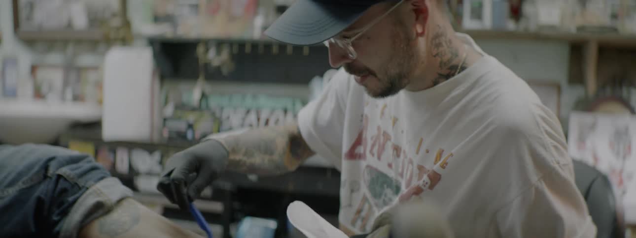A tattoo artist shaves a client's leg before working on it